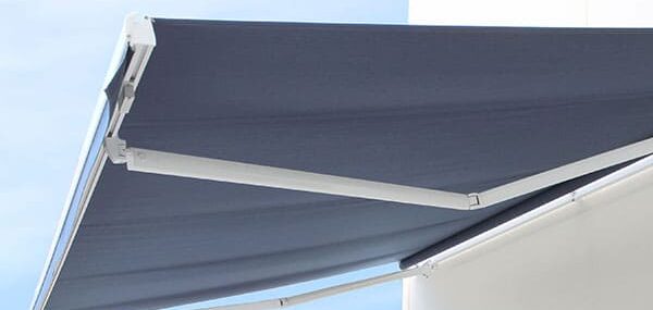 Dark grey folding-arm outdoor awning extended from a white exterior wall against a blue sky.
