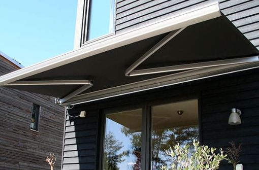 Retractable black outdoor awning extended over patio doors to provide summer shade on a modern home.
