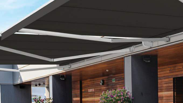 Wide folding arm awnings projection extending over an outdoor entertaining area with timber wall panelling.