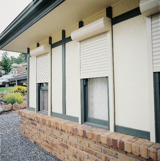 Cream security roller shutters installed on residential exterior windows above a brick sill.